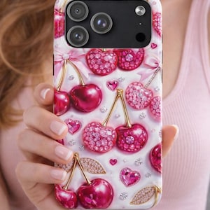 May include: A phone case with a white background, adorned with a pattern of pink cherries, hearts, and gold accents. The cherries are embellished with sparkling pink crystals. The case has a black camera section.
