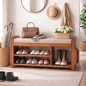 May include: A wooden entryway bench with a beige cushion, shoe storage, and a brown leather handbag. The bench holds various shoes and boots. A round mirror and a hat hang on the wall above the bench.