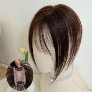 May include: A brown hair topper with a layered fringe, displayed on a mannequin head. The hairpiece has a clip-in design for easy attachment. The hair has highlights and lowlights, creating a natural look. A close-up shows the clip mechanism.