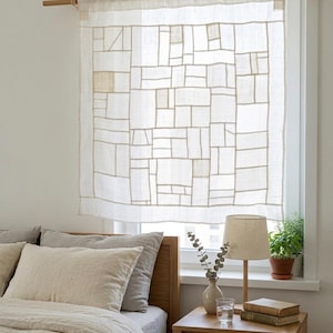 May include: A semi-sheer white linen curtain featuring a geometric patchwork grid pattern of stitched rectangular panels. The curtain is suspended from a light-toned wooden rod and hangs over a window, allowing soft light to filter through the fabric.