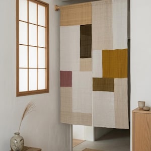 Könnte beinhalten: Ein rechteckiger Türvorhang aus Stoff mit einem Patchwork-Design aus verschiedenen leinenstrukturierten Paneelen in den Farben Creme, Beige, Senfgelb, Olivgrün, Dunkelbraun und gedecktem Mauve, aufgehängt an einer Holzstange.