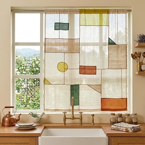 Puede incluir: Una cortina de ventana semitransparente con un diseño de patchwork de tela beige con textura de lino, acentuada con formas geométricas en verde oliva, amarillo mostaza, naranja quemado y verde azulado oscuro, colgada de una barra.