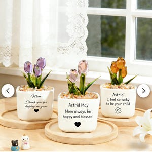 May include: Three small white ceramic pots with glass tulip flowers in shades of purple, pink, and orange. Each pot has a message and a heart or flower symbol. The pots sit on wooden trays.