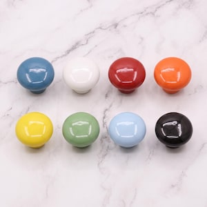 Peut inclure: Un ensemble de huit boutons de placard ronds, lisses et brillants, d&eacute;clin&eacute;s en plusieurs couleurs unies : bleu, blanc, rouge, orange, jaune, vert, bleu clair et noir. Chaque bouton pr&eacute;sente un design simple, uniforme et en forme de champignon.