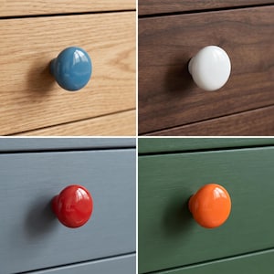 Peut inclure: Un ensemble de quatre boutons de placard ronds en bleu, blanc, rouge et orange, chacun mont&eacute; sur une fa&ccedil;ade de tiroir. Les boutons ont une finition lisse et brillante et sont fix&eacute;s sur des surfaces en bois avec des veines apparentes.