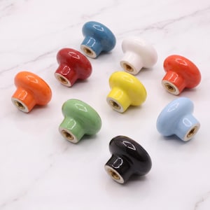 Peut inclure: Un ensemble de neuf boutons de placard ronds en c&eacute;ramique de diff&eacute;rentes couleurs unies, notamment rouge, blanc, orange, jaune, vert, bleu, bleu clair et noir. Chaque bouton pr&eacute;sente une finition lisse et brillante avec un insert filet&eacute; en m&eacute;tal.