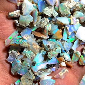 Könnte beinhalten: Eine Ansammlung roher Opal-Edelsteine, die eine Vielzahl von Farben wie Blau, Grün, Orange und Weiß aufweisen. Die unpolierten Steine haben ein natürliches Aussehen mit sichtbaren Texturen und Variationen in Farbe und Opazität. Die Opale sind in verschiedenen Größen erhältlich.