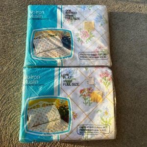 May include: Two packages of No Iron Muslin bed sheets, one fitted and one flat, in full size. The packaging features a white background with a yellow diamond grid pattern and floral motifs. Text includes 50% polyester, 50% cotton, and dimensions.