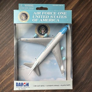 May include: A die-cast metal model of Air Force One, the United States of America presidential aircraft, in a clear plastic display case. The packaging includes the text "AIR FORCE ONE UNITED STATES OF AMERICA".
