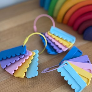 May include: Three sets of scalloped-edge plastic tags in various pastel and primary colors, each attached to a flexible circular ring. The tags feature a flat rectangular body with a decorative wavy edge, organized in a fan-like arrangement on each ring.