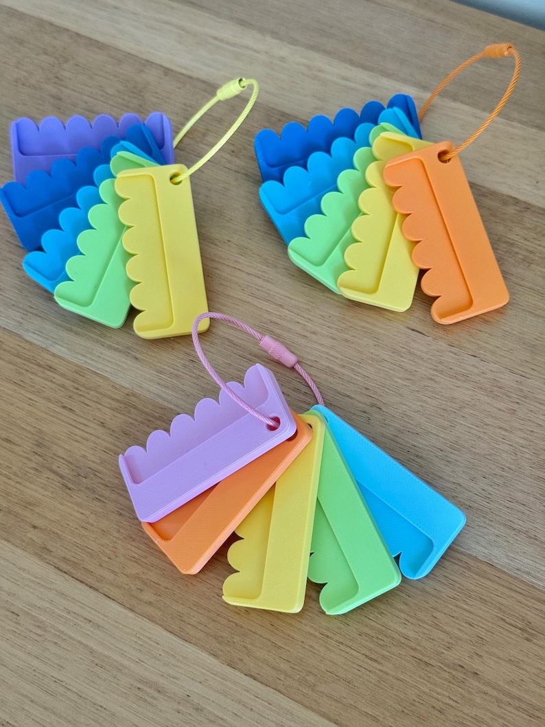 May include: Three sets of plastic yarn bobbins, each featuring a scalloped edge and a central hole for threading. The bobbins are arranged in fan-like clusters on flexible wire loops, showcasing a vibrant spectrum of colors including blue, green, yellow, orange, and purple.