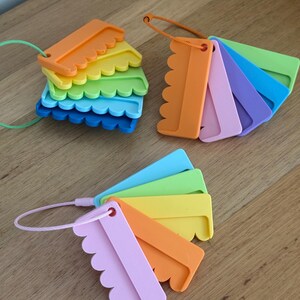 May include: Three sets of plastic color swatches, each featuring multiple rectangular pieces with scalloped edges. The swatches are held together by thin, flexible cables in green, orange, and pink, displaying a variety of vibrant colors.