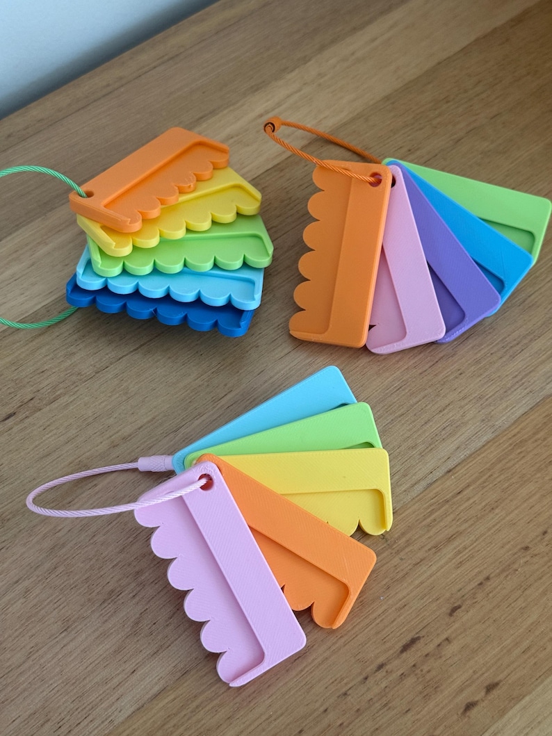 May include: Three sets of plastic color swatches, each featuring multiple rectangular pieces with scalloped edges. The swatches are held together by thin, flexible cables in green, orange, and pink, displaying a variety of vibrant colors.