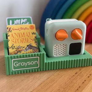 May include: A mint green audio player with orange controls is on a green base, beside a green book holder. The holder contains a book titled "Animal Stories" by Enid Blyton, and a card that says "Little". The name "Grayson" is printed on the holder.