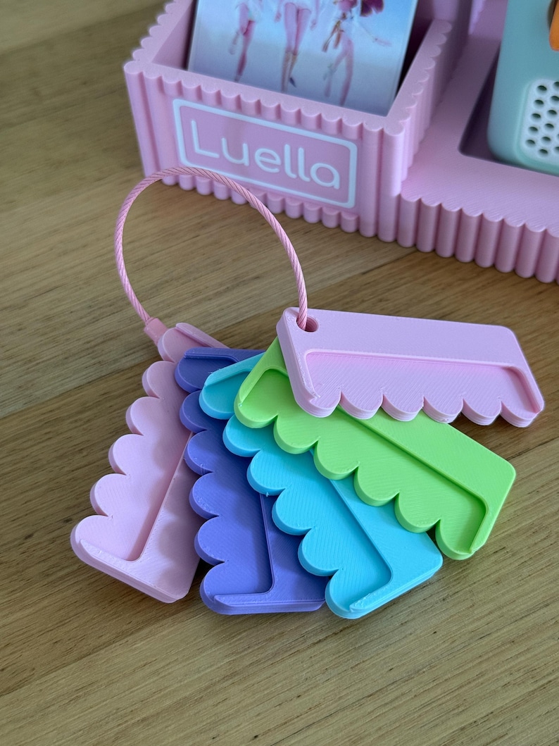 May include: A set of five plastic hair combs in pastel pink, purple, blue, and green, attached to a pink circular wire ring. The combs feature a scalloped edge design and are displayed in front of a pink plastic organizer labeled Luella.