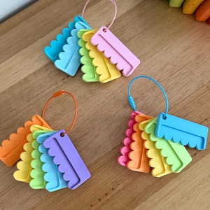 May include: Three sets of plastic scalloped tags in various colors, including pink, yellow, green, blue, orange, and purple. Each set is held together by a flexible metal cable ring, allowing the individual tags to fan out in a circular arrangement.