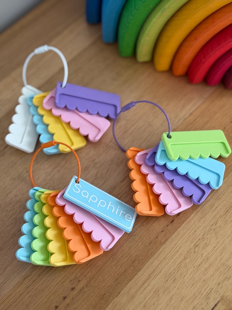 May include: Three sets of colorful, scalloped-edge plastic tags organized on circular rings. The tags come in various shades including blue, green, yellow, orange, pink, and purple. One light blue tag features the word Sapphire printed in white.