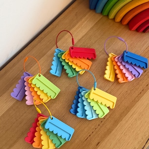 May include: Five sets of colorful, scalloped-edge plastic tags are organized on individual metal rings. Each set features a variety of bright hues including red, orange, yellow, green, blue, and purple, with each tag having a distinct wavy bottom edge.