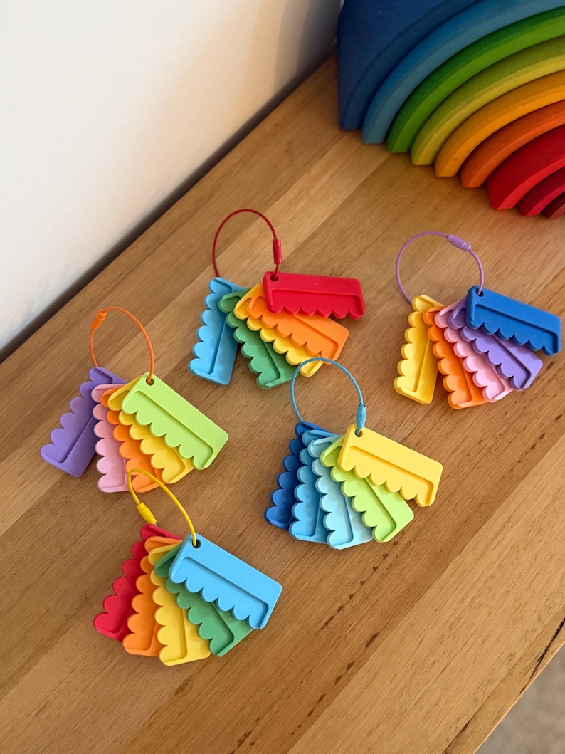 May include: Five sets of colorful, scalloped-edge plastic tags are organized on individual metal rings. Each set features a variety of bright hues including red, orange, yellow, green, blue, and purple, with each tag having a distinct wavy bottom edge.