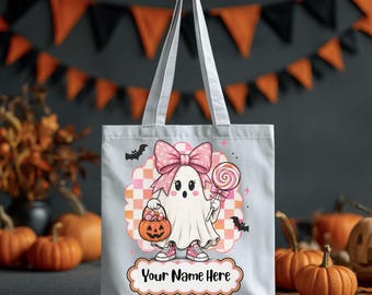 Può includere: Una borsa tote in tela bianca con la grafica di un fantasma che indossa un fiocco rosa a pois e scarpe da ginnastica rosa, che tiene in mano un secchiello a forma di zucca e un lecca-lecca. Il design include uno sfondo a scacchi, pipistrelli e il testo Your Name Here.