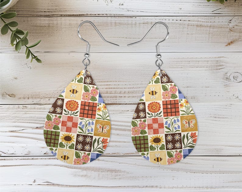 May include: A pair of teardrop-shaped dangle earrings featuring a patchwork pattern of squares. The design includes illustrations of sunflowers, daisies, bluebells, pink flowers, bees, and butterflies in shades of yellow, orange, green, and blue.