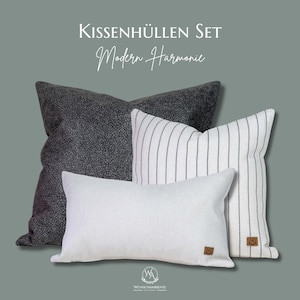 Könnte beinhalten: Ein Set aus vier dekorativen Kissen in verschiedenen Designs. Ein Kissen ist dunkelgrau mit einem strukturierten Muster, ein anderes ist weiß mit vertikalen schwarzen Streifen, und zwei sind einfarbig weiß. Die Kissen sind vor einem grauen Hintergrund angeordnet. Der Text "Kissenhüllen Set Modern Harmonie" steht oben.