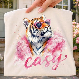 Könnte beinhalten: Beige Tragetasche mit einer Aquarellillustration eines Tigers mit rosa Sonnenbrille und rosa Boa. Das Wort "easy" ist in rosa Schreibschrift unter dem Tiger geschrieben.