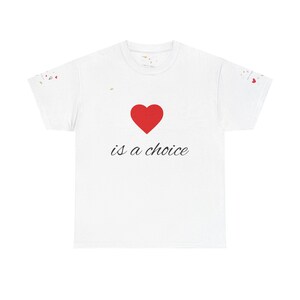 Puede incluir: Camiseta blanca con un corazón rojo y la frase "is a choice" en cursiva. Las mangas tienen pequeños diseños de confeti de colores. Una prenda casual y cómoda, ideal para el uso diario.