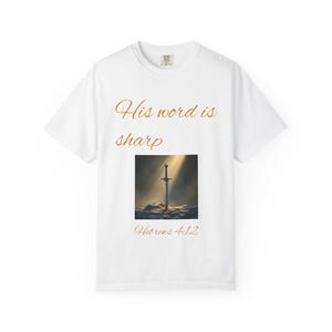 May include: White t-shirt featuring the gold text "His word is sharp". Beneath this is a square image of a sword in a stone, illuminated by a ray of light. The text "Hebrews 4:12" is below the image, all in gold.