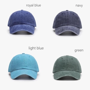 May include: Four baseball caps in royal blue, navy, light blue, and green. Each cap has a curved brim and a fabric strap closure. The caps are displayed against a white background, with the color names above each cap.