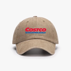 May include: A tan baseball cap with the Costco Wholesale logo in red and blue. The hat has a curved brim and an adjustable strap at the back. The logo is centered on the front of the cap.