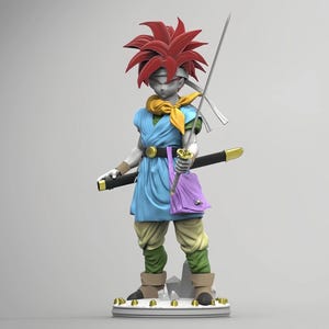 Op de afbeelding: Gedetailleerd beeldje van een personage met stekelig rood haar, gekleed in een blauwe tuniek, gele sjaal en beige broek. Het figuur houdt een zwaard en een schede vast. Een paarse tas hangt aan de taille van het personage. De basis is versierd met gouden accenten.
