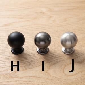 以下が含まれることがあります： H、I、Jとラベル付けされた3つの球状のキャビネットノブ。ノブHはマットブラック、ノブIはダークメタリックグレー、ノブJはつや消しシルバー仕上げです。各ノブは丸いヘッドと円形のベースを備えており、横一列に並んでいます。