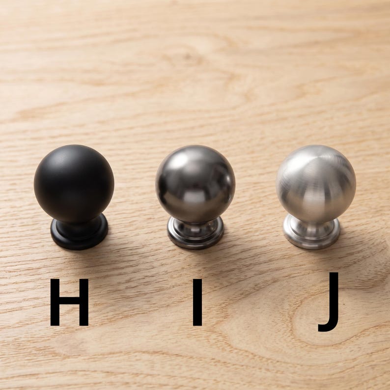 以下が含まれることがあります： H、I、Jとラベル付けされた3つの球状のキャビネットノブ。ノブHはマットブラック、ノブIはダークメタリックグレー、ノブJはつや消しシルバー仕上げです。各ノブは丸いヘッドと円形のベースを備えており、横一列に並んでいます。