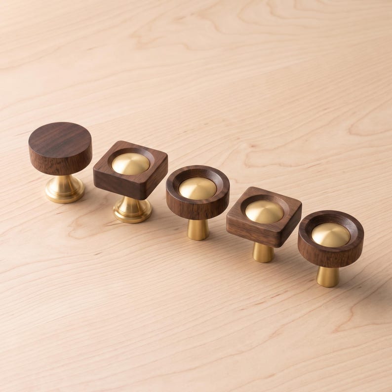 May include: A set of five cabinet knobs featuring dark brown wood and polished brass metal components. The collection includes circular and square wooden bases, each centred with a smooth, rounded brass inlay and supported by a brass pedestal.