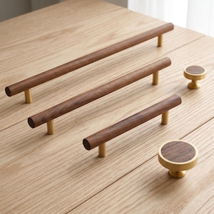 May include: A collection of cabinet hardware featuring three cylindrical wooden drawer pulls of varying lengths and two circular wooden knobs, all accented with brushed brass metal mounting posts and circular bases for attachment.