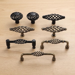 May include: A collection of seven cabinet hardware pieces including two round knobs, three T-bar pulls, and two arch-style handles. The hardware features a mix of matte black and antique brass finishes, all showcasing a distinct twisted wire cage design.