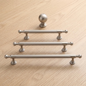 May include: A set of four brushed nickel cabinet hardware pieces consisting of one spherical knob and three horizontal bar pulls of varying lengths. Each pull features a central ribbed texture with smooth rounded ends and two mounting posts.