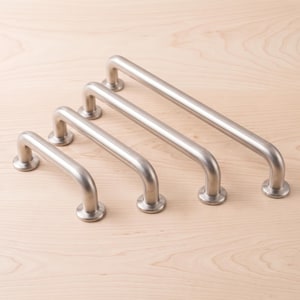 Könnte beinhalten: Vier gebürstete silberne Metall-Schrankgriffe, die in einer diagonalen Reihe von kurz nach lang angeordnet sind. Jeder Griff besteht aus einer glatten, zylindrischen Stange mit abgerundeten Enden und zwei runden Montagebasen.