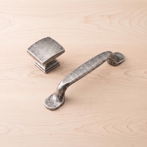 May include: A square cabinet knob and a matching arched drawer pull handle, both featuring a distressed, weathered silver-toned metal finish with a textured, mottled surface appearance and a solid, sturdy construction for furniture hardware.