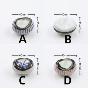 以下が含まれることがあります： A、B、C、Dとラベル付けされた4つの陶磁器製箸置き。各楕円形の箸置きは40mm x 30mmのサイズです。Aは青いストライプ、Bは黒い帯、Cは青い花柄、Dは赤いストライプと濃い茶色の縁取りが特徴です。