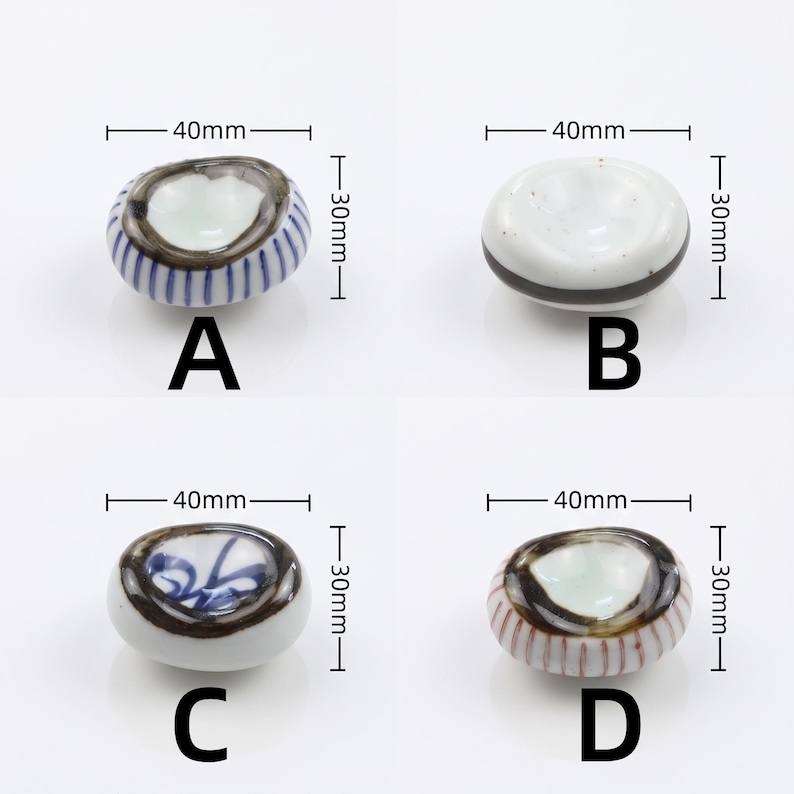 以下が含まれることがあります： A、B、C、Dとラベル付けされた4つの陶磁器製箸置き。各楕円形の箸置きは40mm x 30mmのサイズです。Aは青いストライプ、Bは黒い帯、Cは青い花柄、Dは赤いストライプと濃い茶色の縁取りが特徴です。