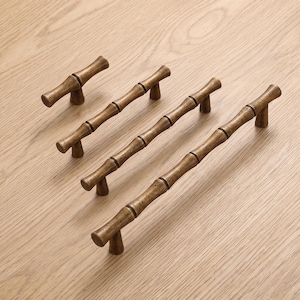 May include: Four metal cabinet pulls with a brushed antique brass finish, each designed to resemble a segmented bamboo stalk. The hardware pieces vary in length, featuring two mounting posts each, and are arranged diagonally in a row.