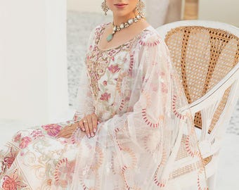 May include: A white embroidered dress with pink and gold floral patterns. The dress features long sleeves and a sheer overlay. The model is wearing a matching necklace and earrings. The dress is suitable for special occasions.