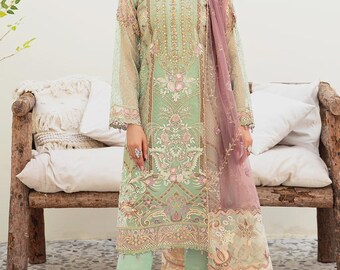 May include: A mint green embroidered ensemble featuring a long-sleeved tunic, matching pants, and a sheer, mauve dupatta. The outfit is adorned with intricate floral patterns and embellishments. The model is wearing a matching necklace and earrings.