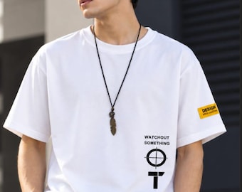 May include: A white short-sleeved t-shirt featuring a black graphic print with the text WATCHOUT SOMETHING and WATCHING SOMETHING alongside crosshair symbols. A small yellow rectangular patch on the left sleeve displays the text DESIGN STYLE COLLECTION.