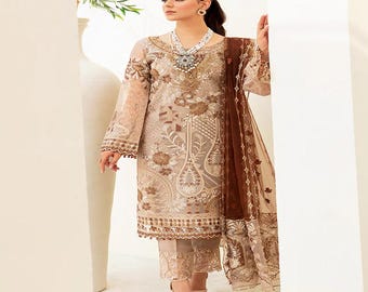 May include: A beige embroidered formal dress with a matching scarf. The dress features intricate floral patterns and long sleeves. The outfit includes matching pants and is worn with light-colored sandals. The dress is a formal wear ensemble.