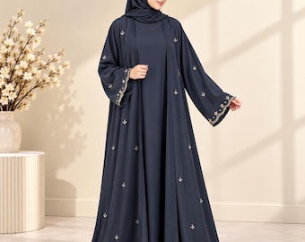 May include: A dark navy blue abaya featuring a matching headscarf and a long, open-front outer layer. The garment is adorned with small, scattered gold embroidered floral motifs and detailed gold embroidery along the wide sleeve cuffs.