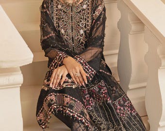 May include: A black embroidered outfit featuring a long-sleeved top and matching pants. The ensemble is adorned with intricate gold and red floral patterns. The model is wearing a white choker necklace and matching earrings. The outfit is suitable for special occasions.
