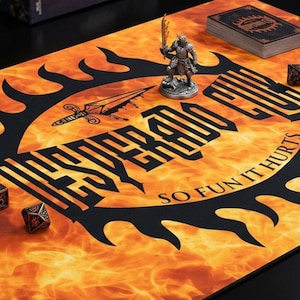 Könnte beinhalten: Spielmatte mit feurigem orange-gelbem Hintergrund, mit dem Text "WESPERADO" und "SO FUN IT HURTS" in Schwarz. Eine Miniaturfigur, Würfel und ein Kartenspiel befinden sich auf der Matte.